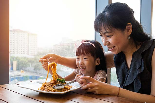 Mom helping her daughter eat spaghetti